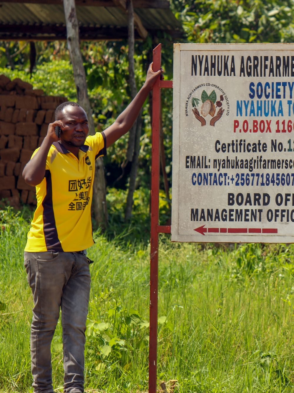 A cooperative member beside the Nyahuka Agrifarmers Cooperative signboard